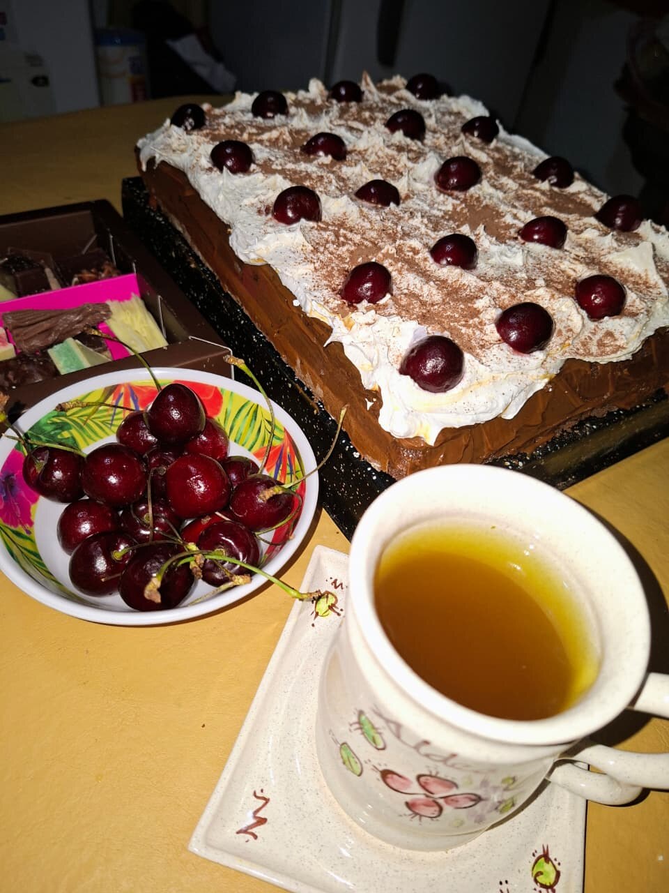 Torta selva negra con cerezas, un bowl de cerezas y una taza de té